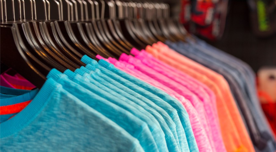 A row of short-sleeve t-shirts displayed in a store. The shirts are hanging neatly and organized by color.
