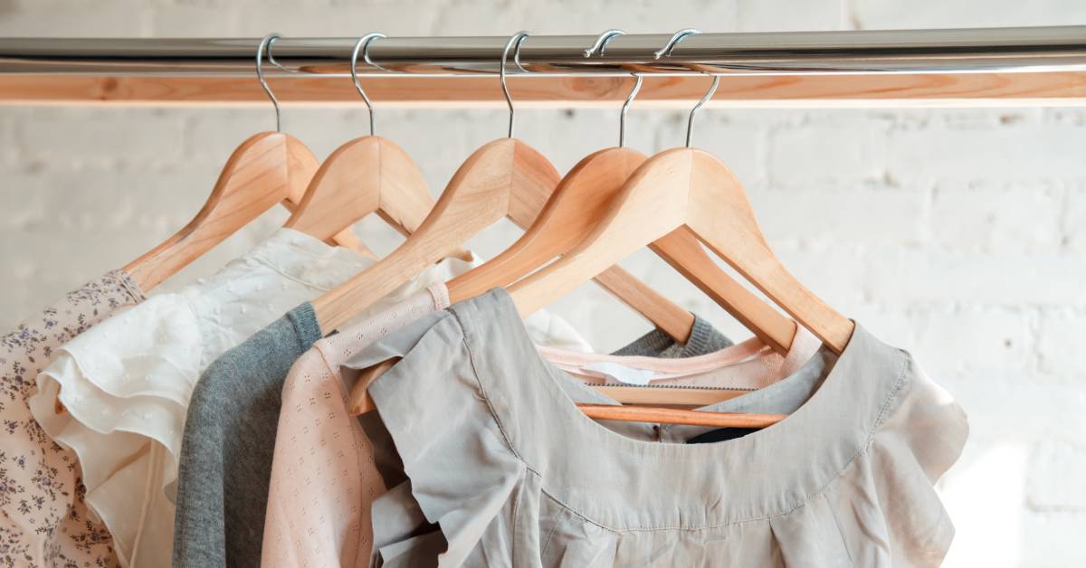 A variety of women's tops are hanging from a metal clothing rack. The lightweight tops are pink, white, and gray.