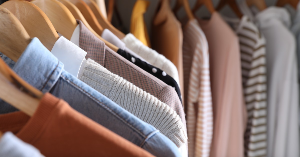 A close-up view of a variety of shirts, sweaters, and blazers hanging from wooden hangers in a closet.