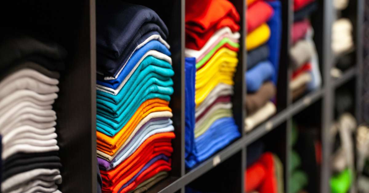 Stacks of folded t-shirts in a black modular storage display. There are stacks of neutral shirts and colorful shirts.