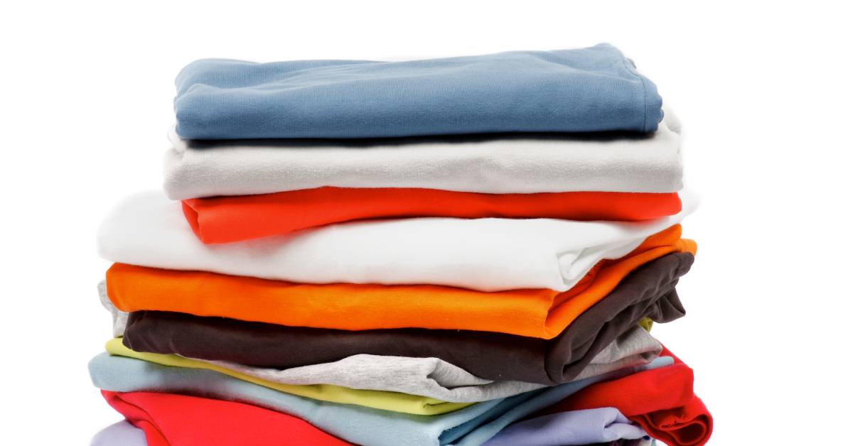 A stack of folded shirts against a white background. The shirts are a variety of colors, including blue, red, and orange.