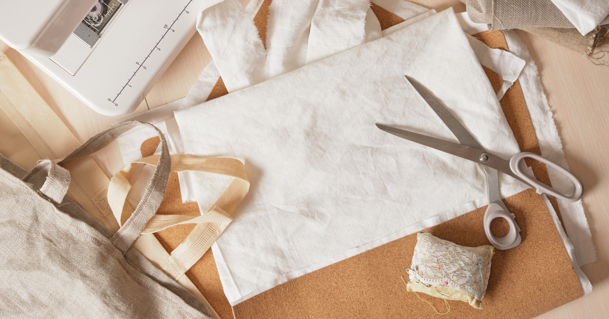 Fabric scraps, a pin cushion, a pair of scissors, and two tote bags are sitting next to a sewing machine.