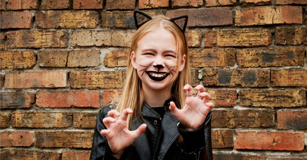 A young girl is dressed in a black cat costume. She is wearing a pair of cat ears and has whiskers drawn on her face.